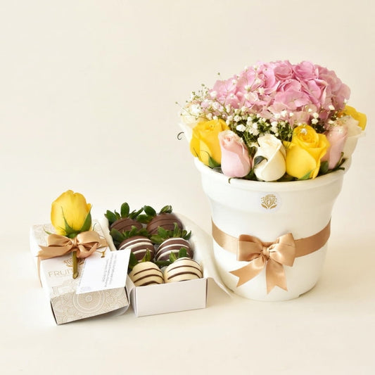 Arreglo de flores y rosas en tonos pastel en base blanca junto a caja de 6 fresas con chocolate